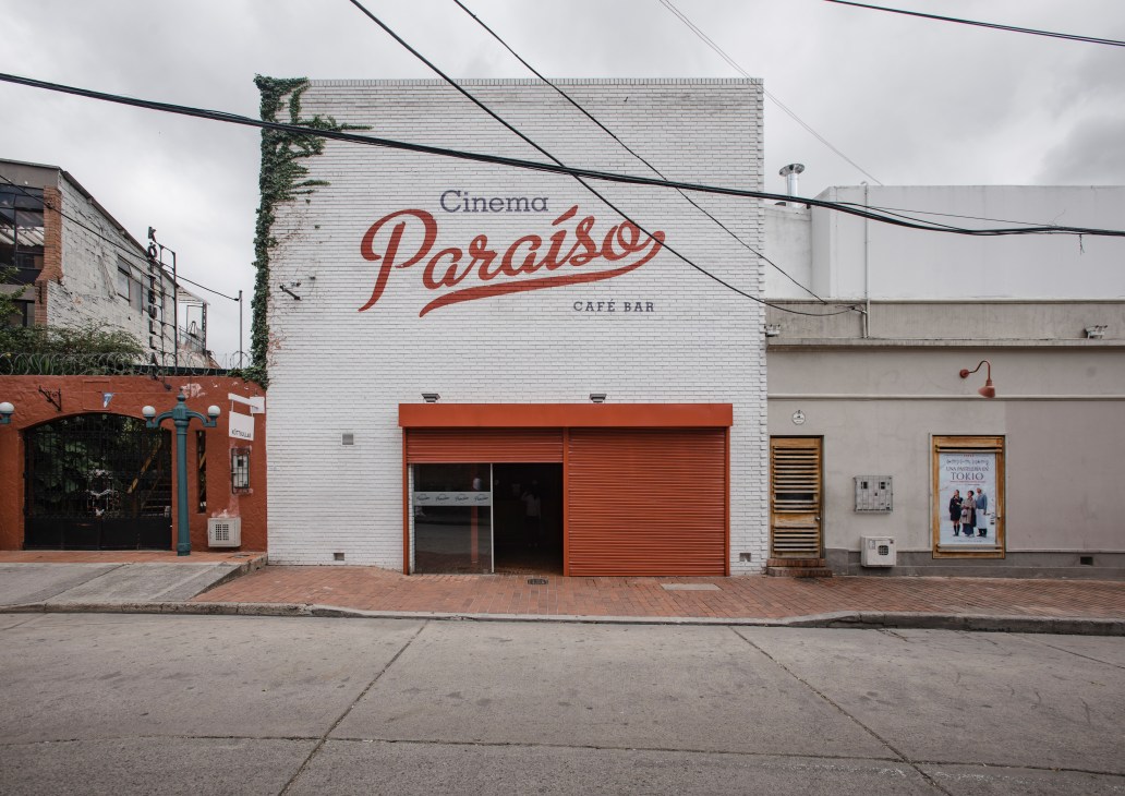 Cinema Paraíso storefront with white brick facade, red signage, and red metal garage doors in Usaquén, Bogotá.