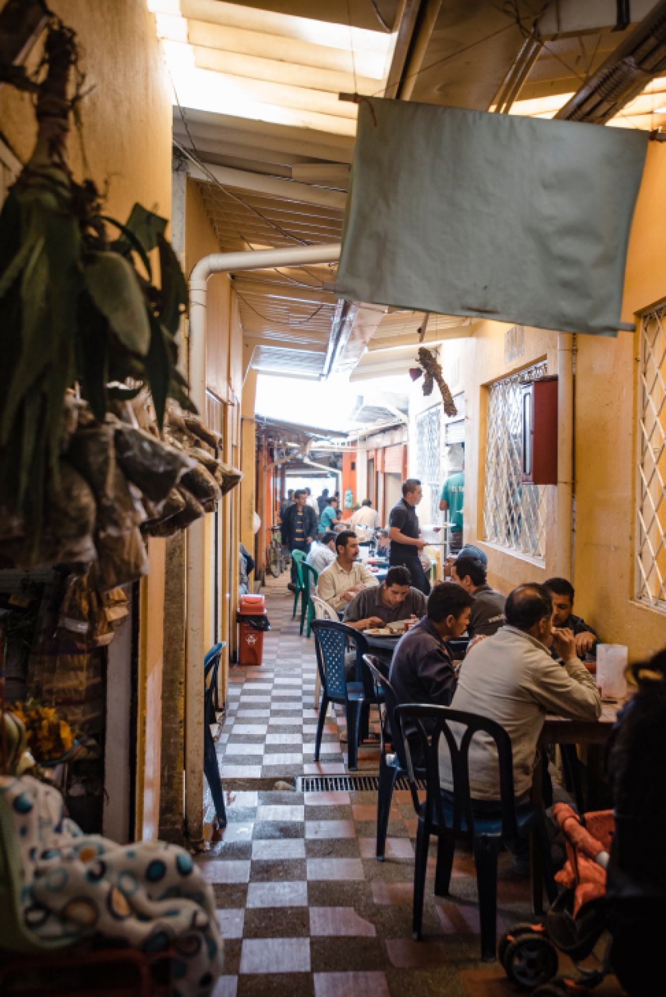People dining at tables in a narrow covered market passageway with yellow walls and skylights.