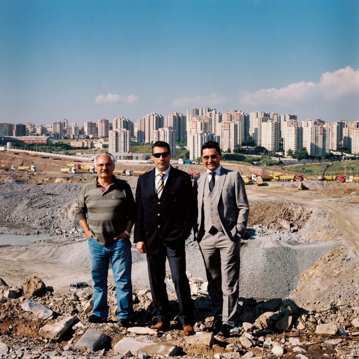 Three men stand in an excavation pit with Istanbul's skyline visible behind them.