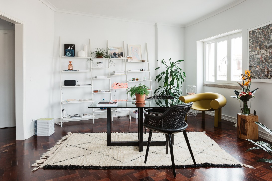 Bright Lisbon apartment interior with white shelving, black table, gold chair and potted plants.