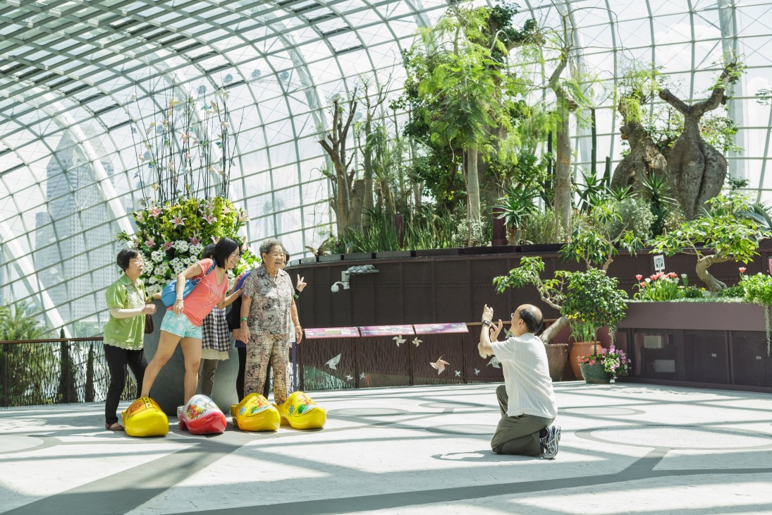 Visitors posing for photos inside a glass-domed conservatory at Gardens by the Bay with tropical plants and trees overhead.