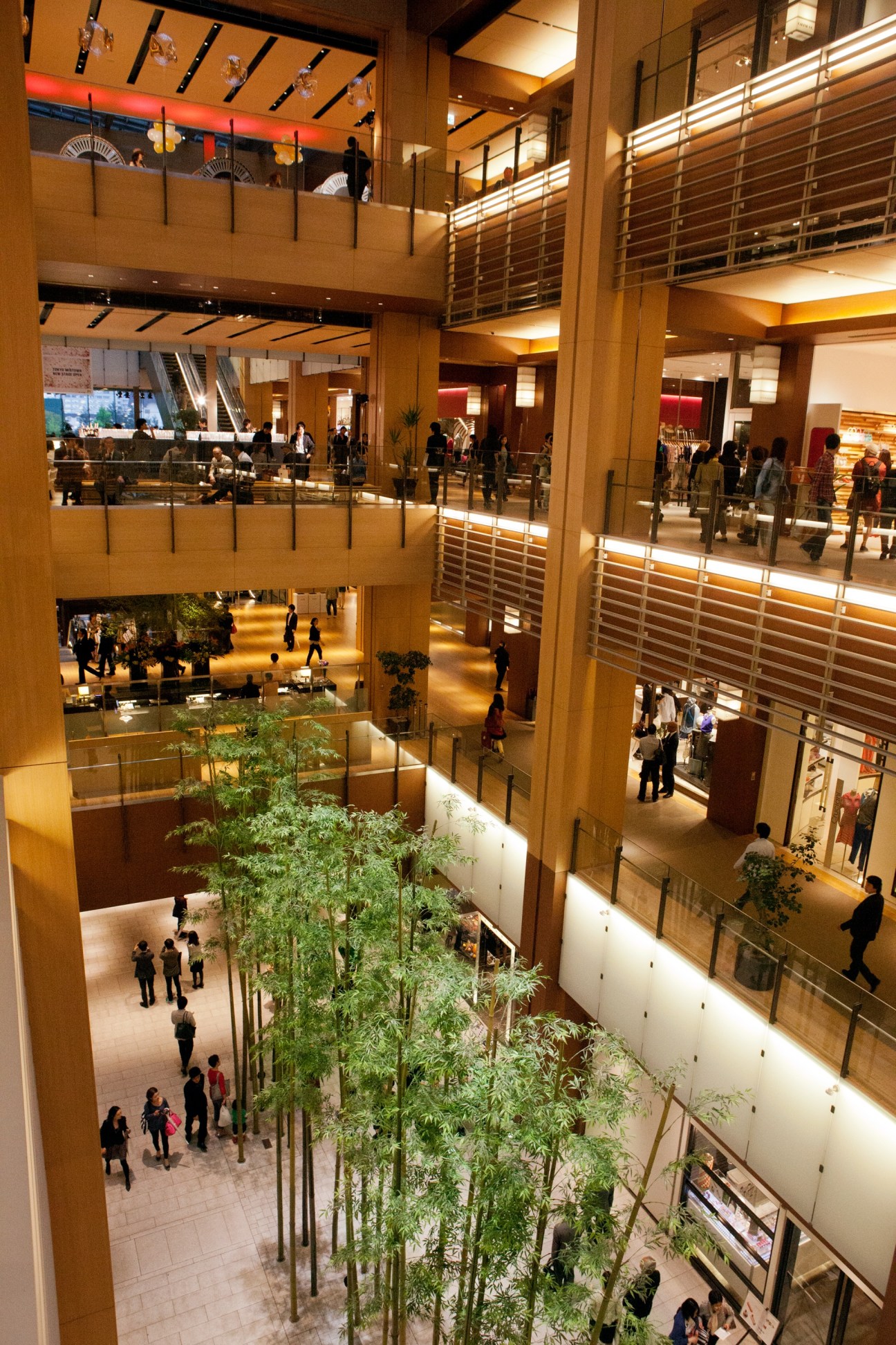 Interior view of Tokyo Midtown shopping complex showing three levels with bamboo plants, wooden architectural elements, and shoppers.
