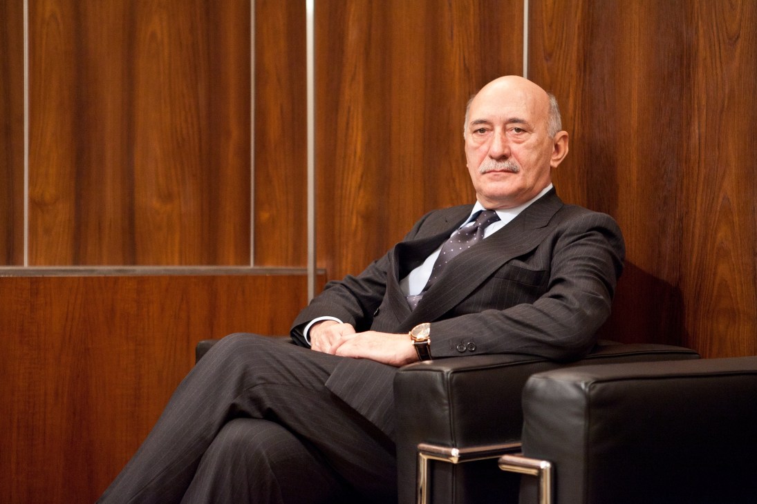Angelo Bonati, CEO of Panerai, sitting on a black leather bench against wood paneling.