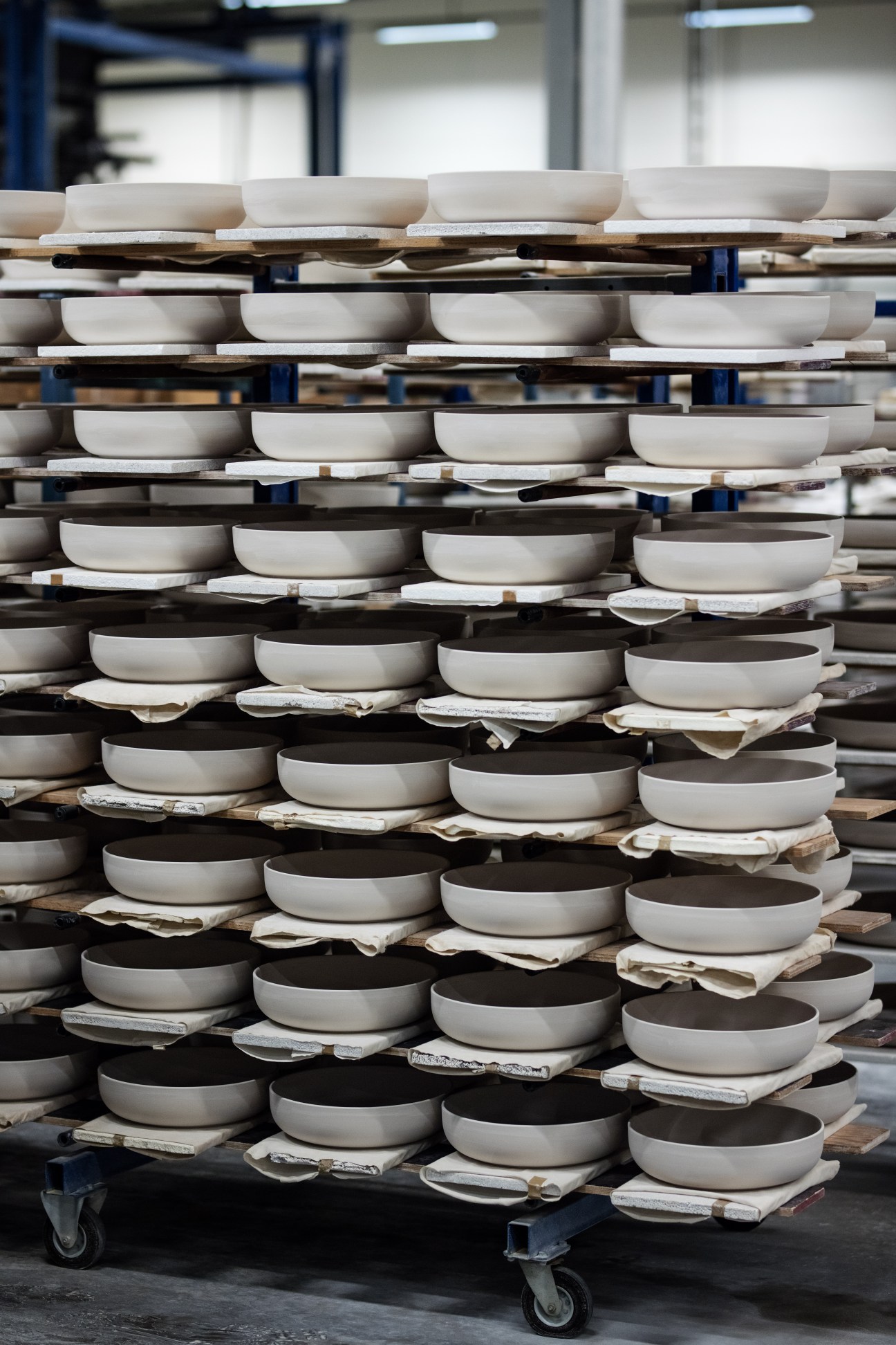 Stacks of white and dark glazed porcelain bowls arranged on wooden shelves with separators in a Figgjo factory cart.