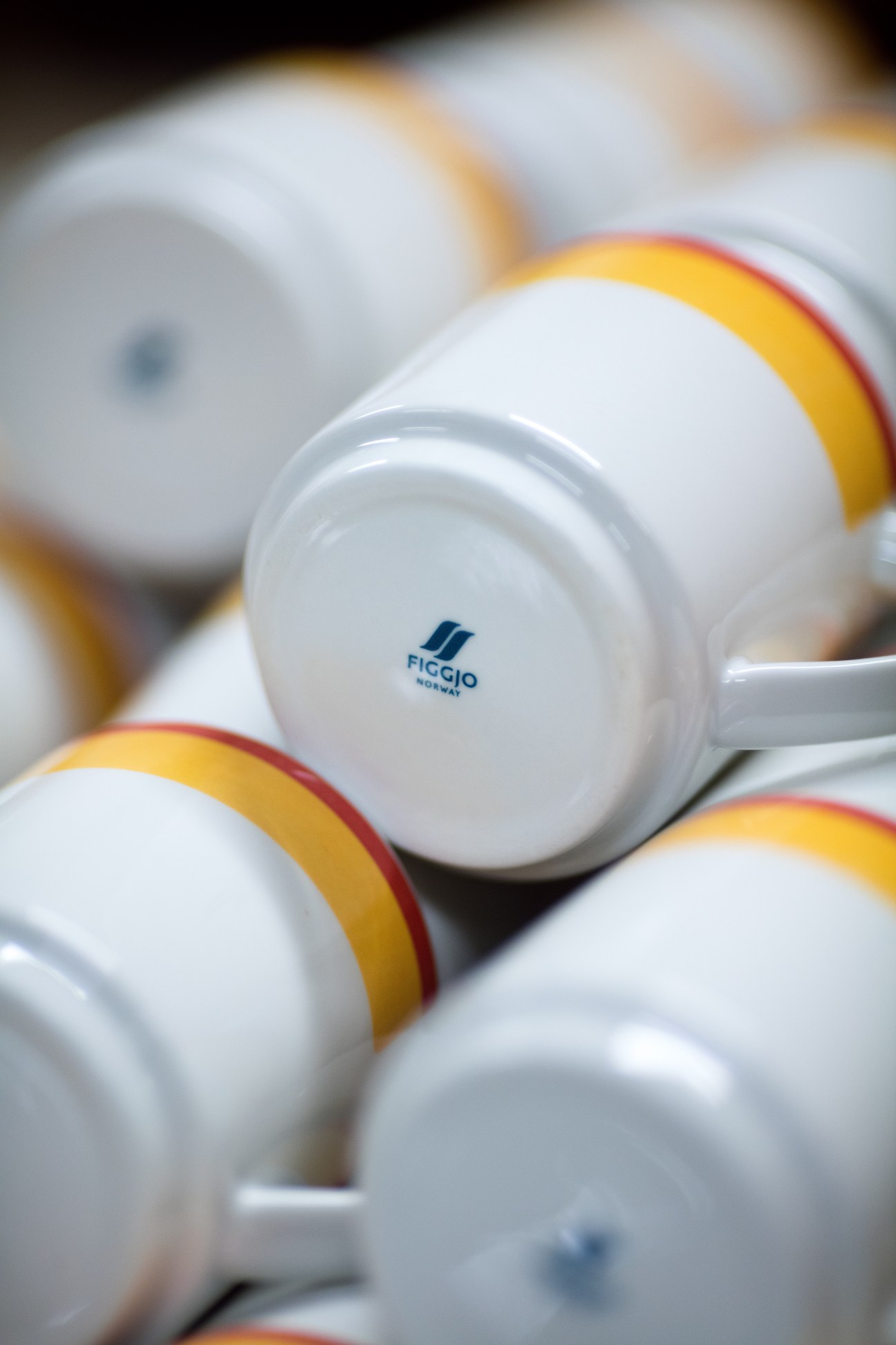 Close-up of white Figgjo porcelain cups with yellow and red band trim showing the Figgjo logo on the base.
