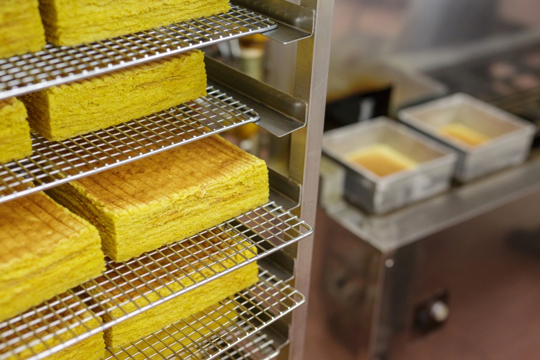 Bright yellow kueh lapis cakes cooling on metal racks in a bakery kitchen.