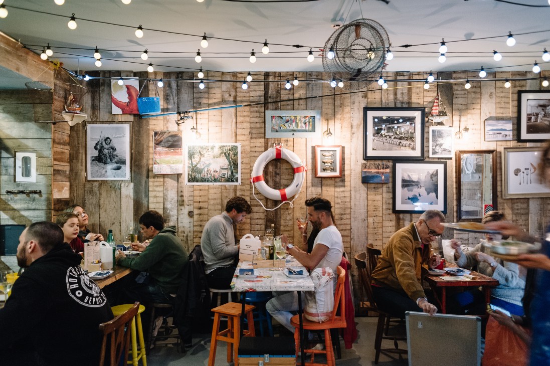 Diners seated at wooden tables in Isco restaurant with rustic wooden wall decorated with framed photographs and maritime objects.