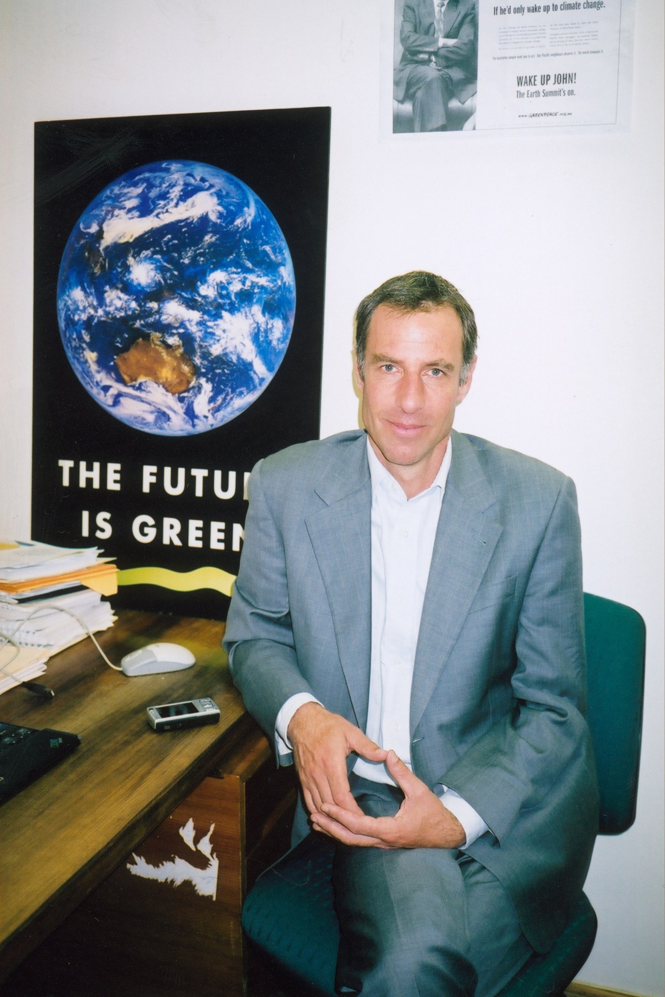 Nick McKim, Tasmanian Greens MP, seated at his desk with environmental posters behind him.