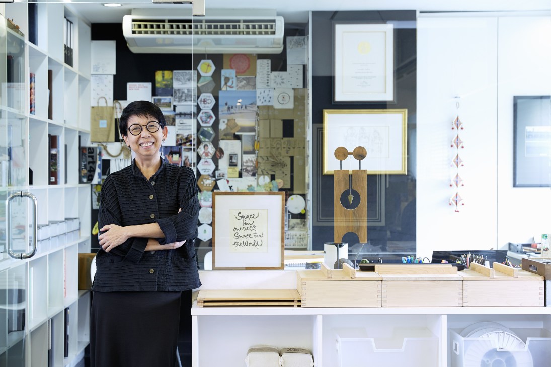 Thai architect Kanika R'kul smiling in her design studio surrounded by inspiration boards and architectural models.