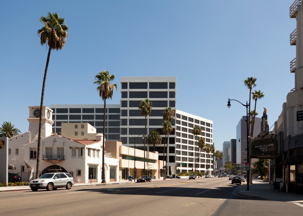 Beverly Hills street with palm trees, historic clock tower building, and modern office buildings under clear blue sky.