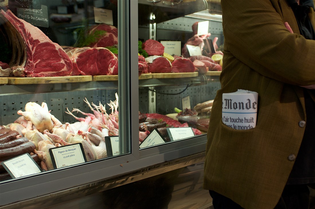 Butcher shop display window at Terroirs d'Avenir with cuts of meat and poultry, person in olive jacket viewing.