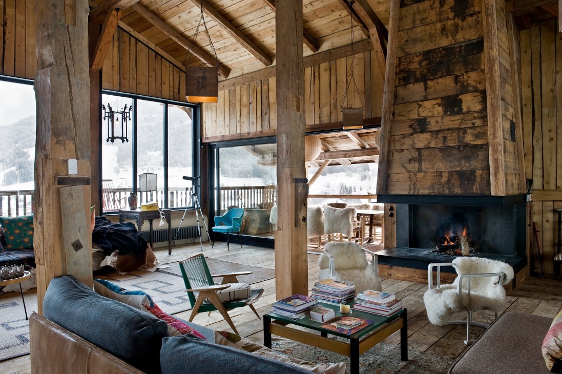 Spacious open-plan living area with soaring wooden ceilings, fireplace, vintage furniture, and mountain views through large windows.