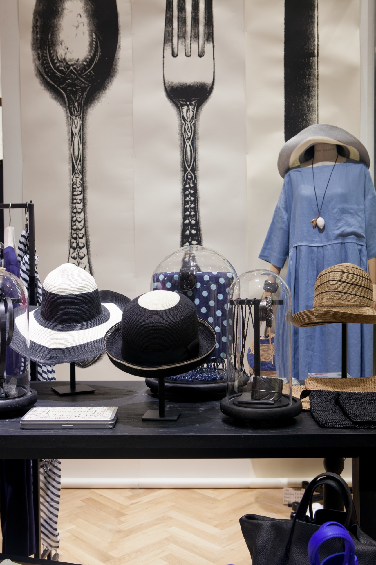 Plain People store window display with hats, accessories, and blue dress against wall with fork and spoon illustration.