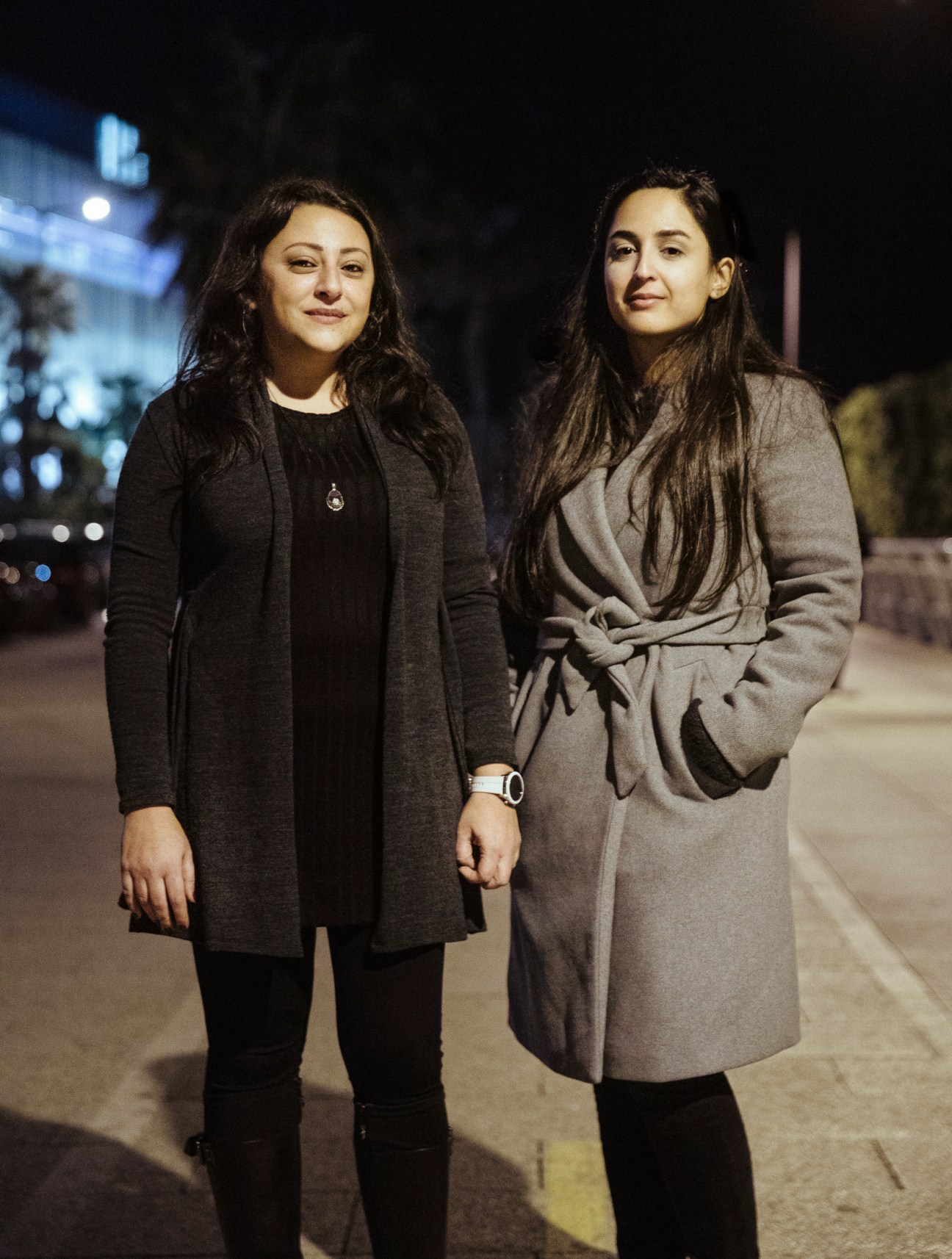 Two women in coats standing together at night on a street