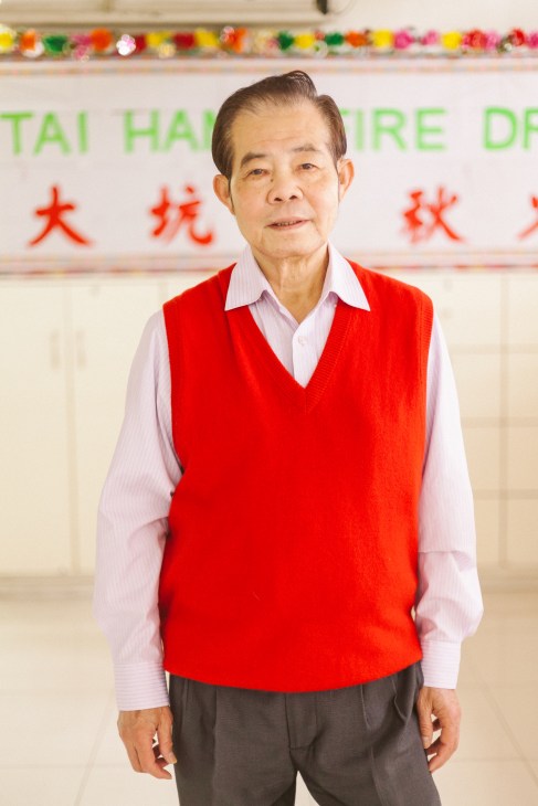 Chan Tak-fai, a Tai Hang resident, poses for a portrait wearing a red vest over a pink shirt.