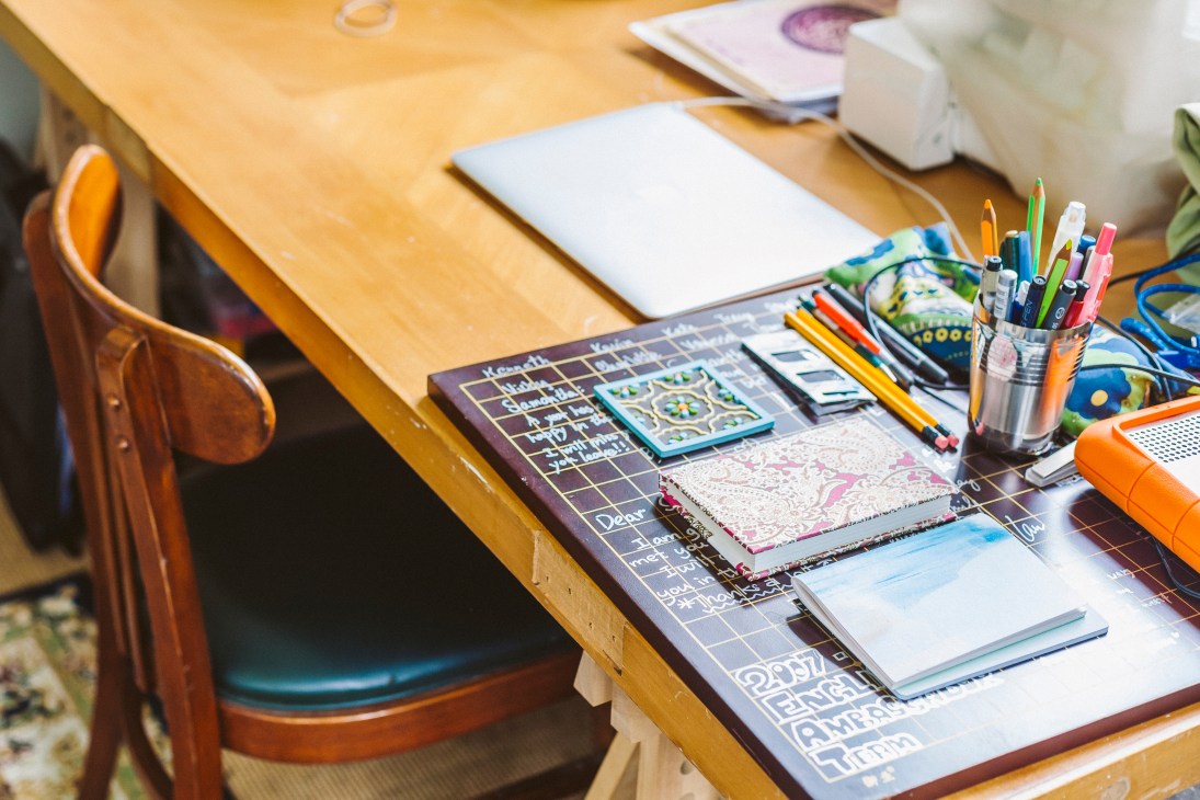 Artist's wooden desk with sketchbooks, colored pencils, markers, and art supplies arranged on surface