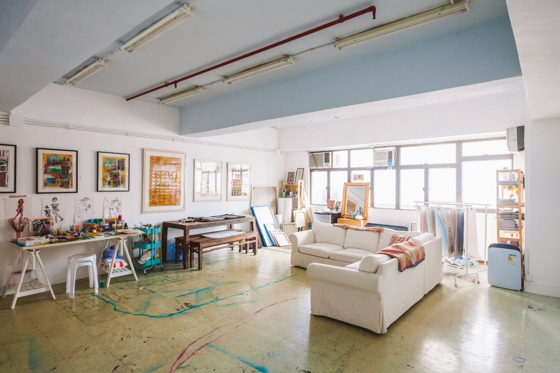 Artist's desk cluttered with papers, sketches, and art supplies in a bright studio space.