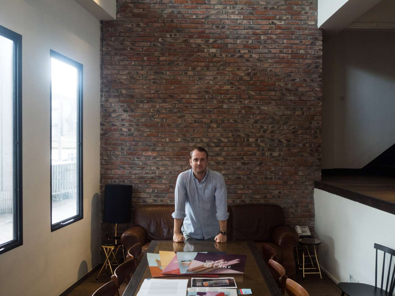 Alexander Bent standing at a desk in a modern office with exposed brick walls and large windows.