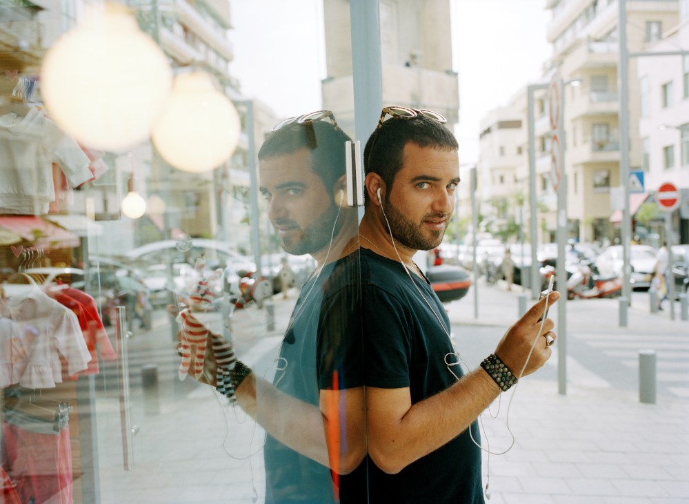 Young man with earbuds and sunglasses on his head reflected in a shop window on Shenkin Street, Tel Aviv.
