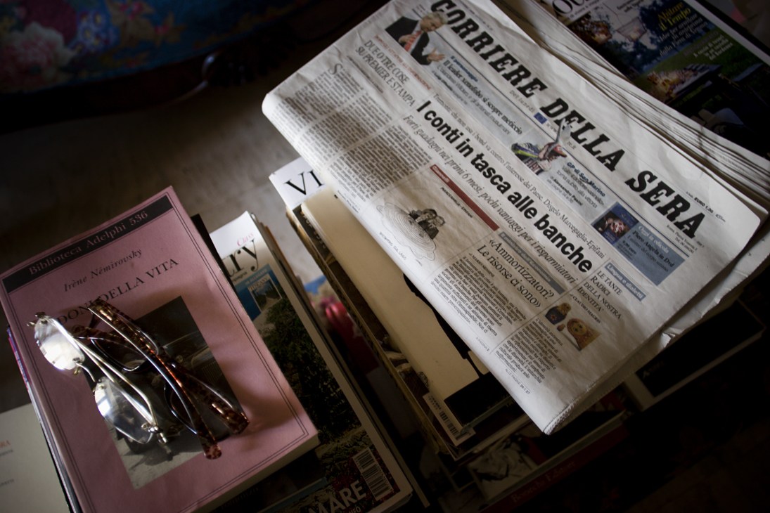 Corriere della Sera newspaper with Emilio Giannelli's cartoon on the front page, displayed with reading glasses and a book.