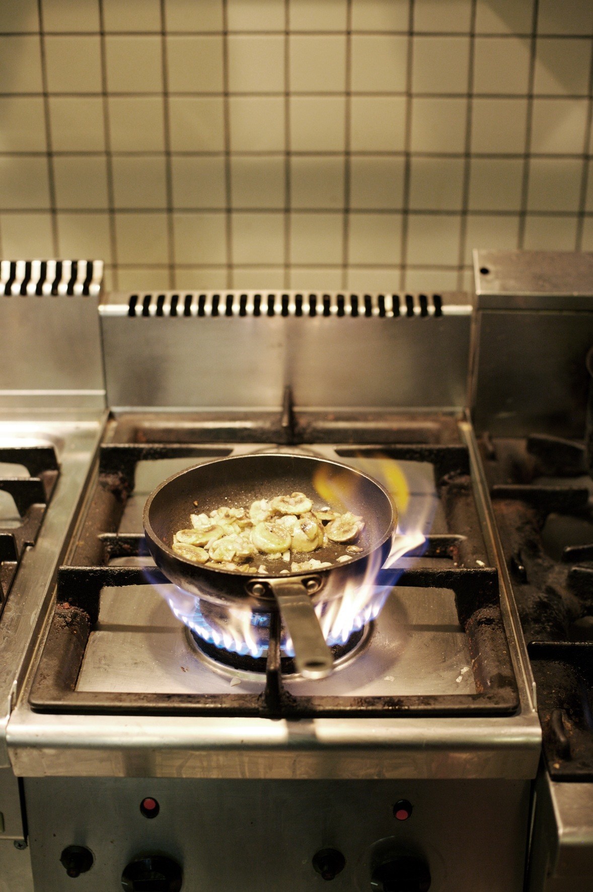 Sliced bananas frying in a pan over a gas flame in a commercial kitchen.