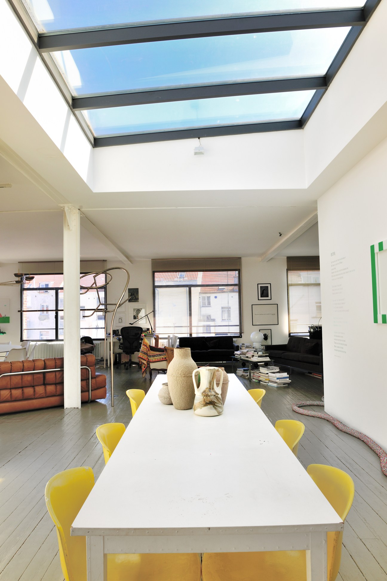 Modern loft interior with white dining table, yellow chairs, large skylight, and contemporary furnishings.