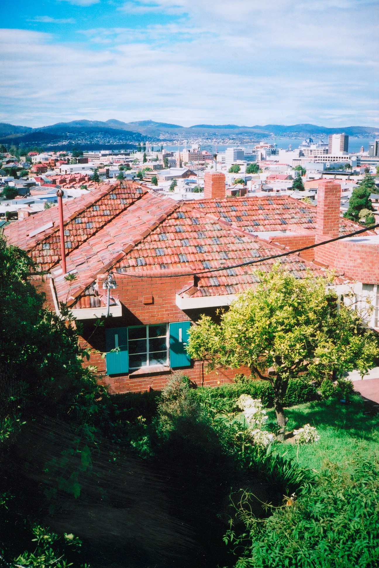 Aerial view over Hobart showing terracotta-roofed houses with city skyline and mountains beyond.
