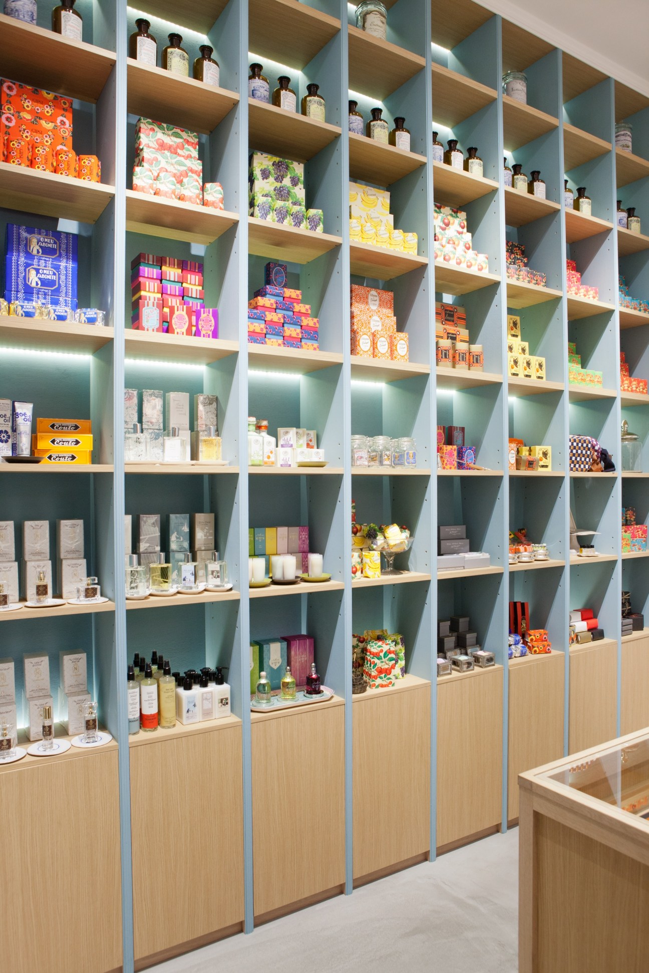 Shelving display at Heroomtage Deux with colorful packaged products, fragrances, and decorative items arranged in turquoise cubicles.