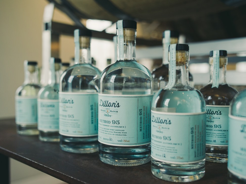 Bottles of Dillon's Method 95 unfiltered gin with turquoise labels displayed on a shelf.