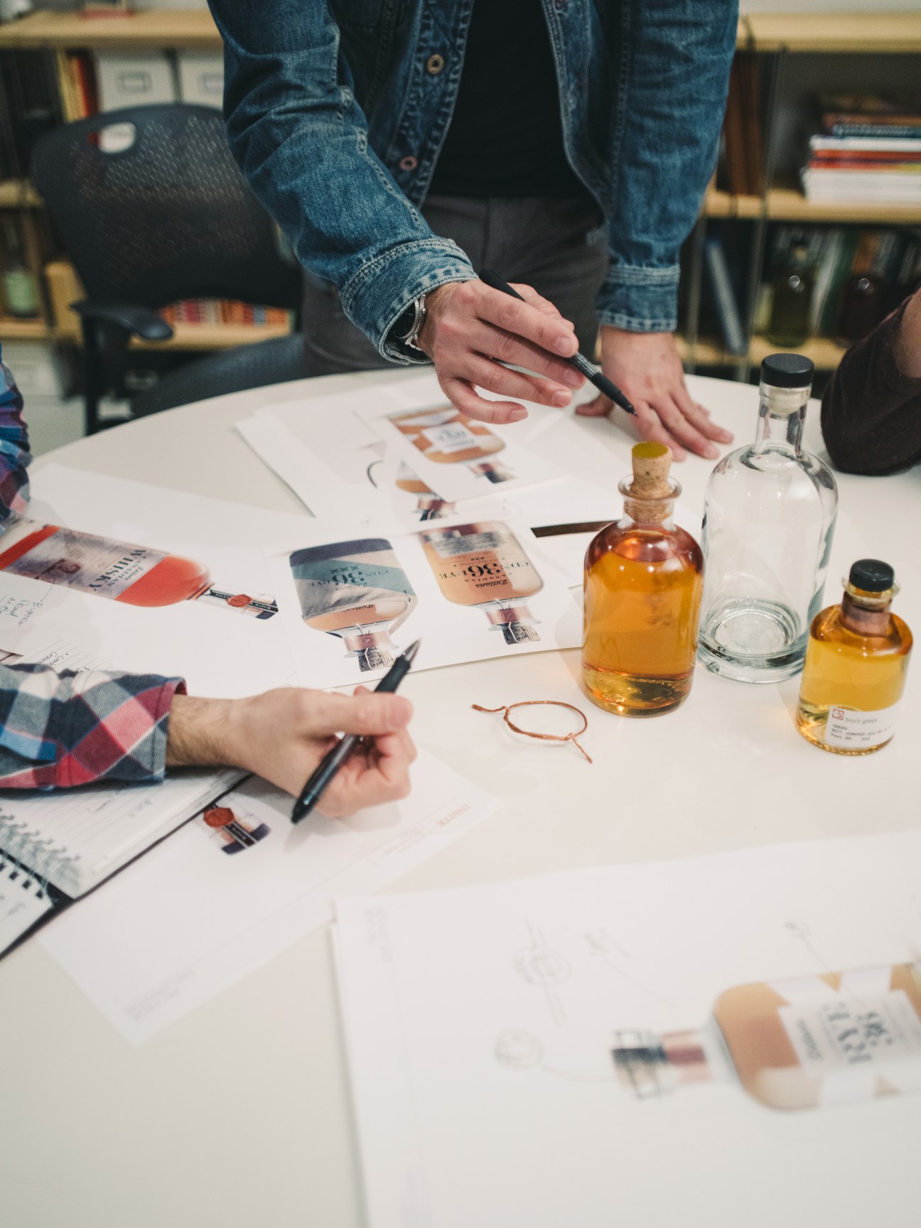 Hands examining spirit bottles and design sketches on a table during packaging development.