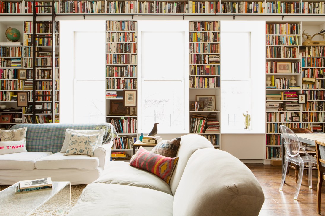Living room with floor-to-ceiling bookshelves, white sofas, and large windows in a Brooklyn loft by Elizabeth Roberts.