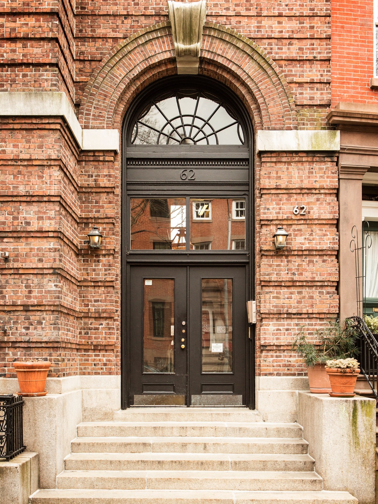 Red brick townhouse facade with black arched doorway featuring fanlight window and number 62.