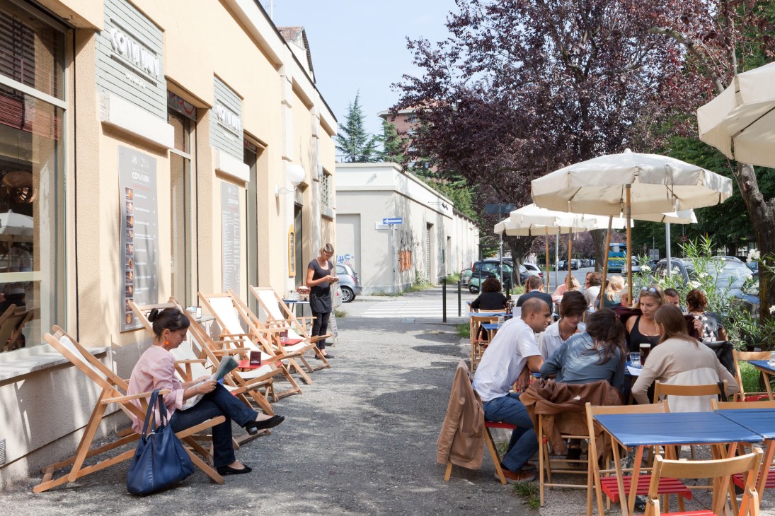 People dining and relaxing at outdoor tables under umbrellas at Convivium riverside café in Turin's Borgo Rossini neighbourhood.