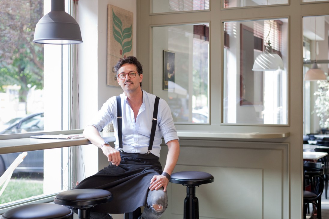 Giovanni Moreno Mazzurco, barista at Convivium, sitting by a window in a bright café interior with industrial pendant lighting.