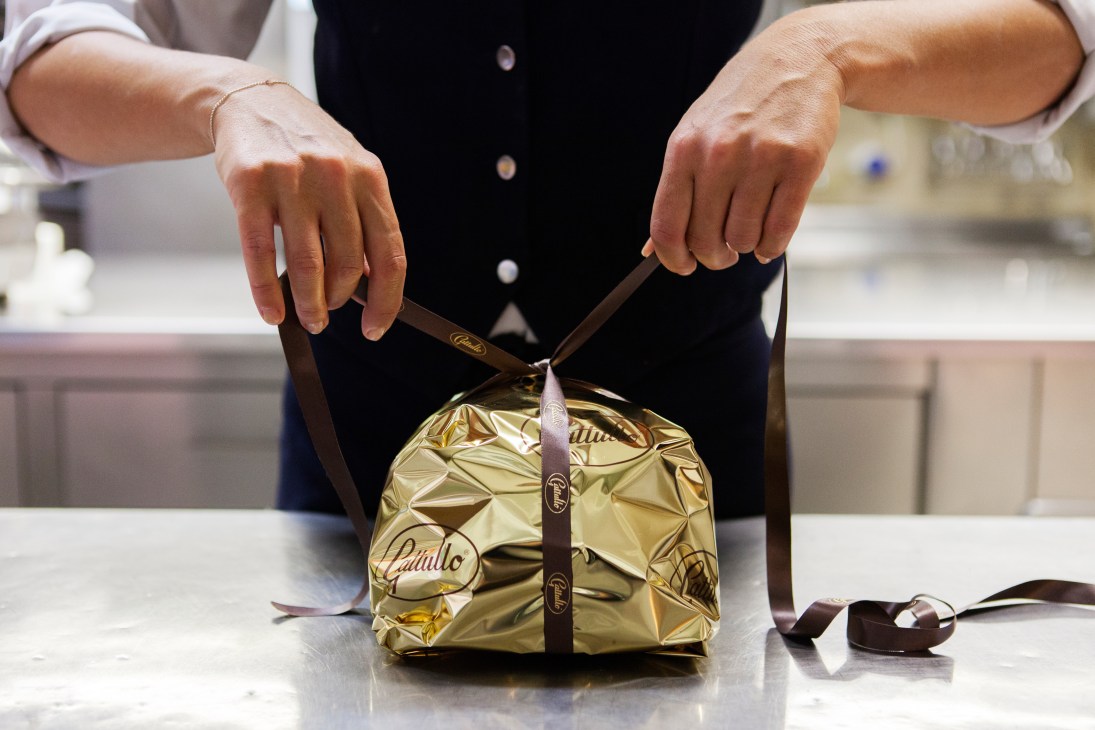 Hands tying a brown ribbon around a gold-wrapped Gattullo panettone package.