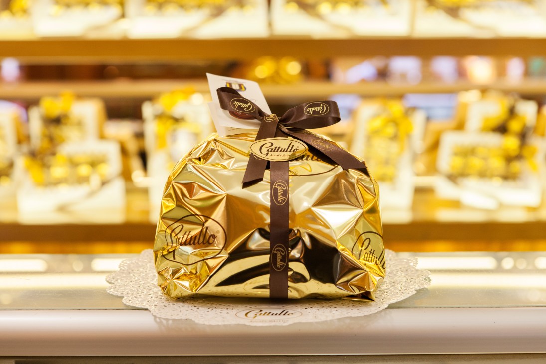 Gattullo panettone wrapped in gold foil with brown ribbon bow displayed in bakery window.