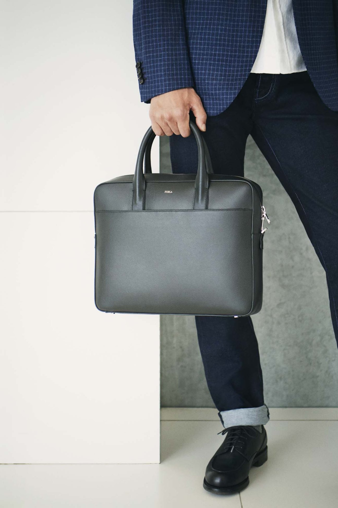 Man in blue blazer and jeans carrying a grey leather briefcase by Furla