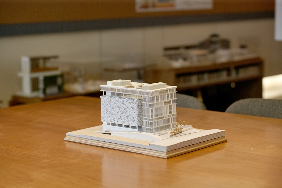 Architectural model of a modern building with textured white facade and grid pattern displayed on wooden base.