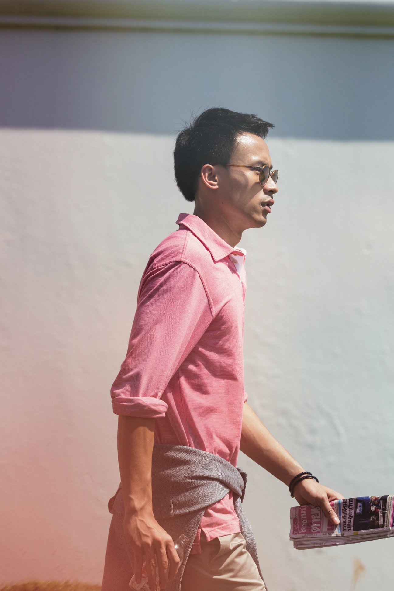 Man in pink polo shirt and Persol sunglasses standing against colorful wall in Bangkok.