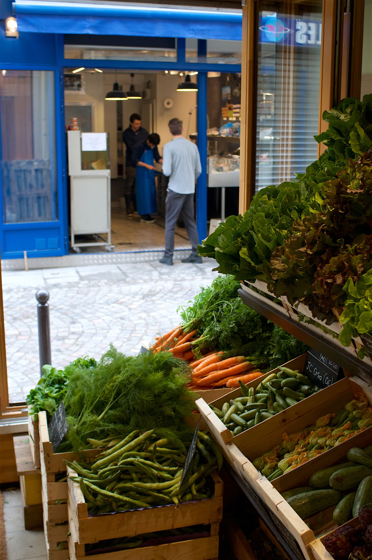 Produce display outside Terroirs d'Avenir greengrocer on Rue du Nil in Paris, featuring fresh vegetables including carrots, beans and cucumbers in wooden crates.