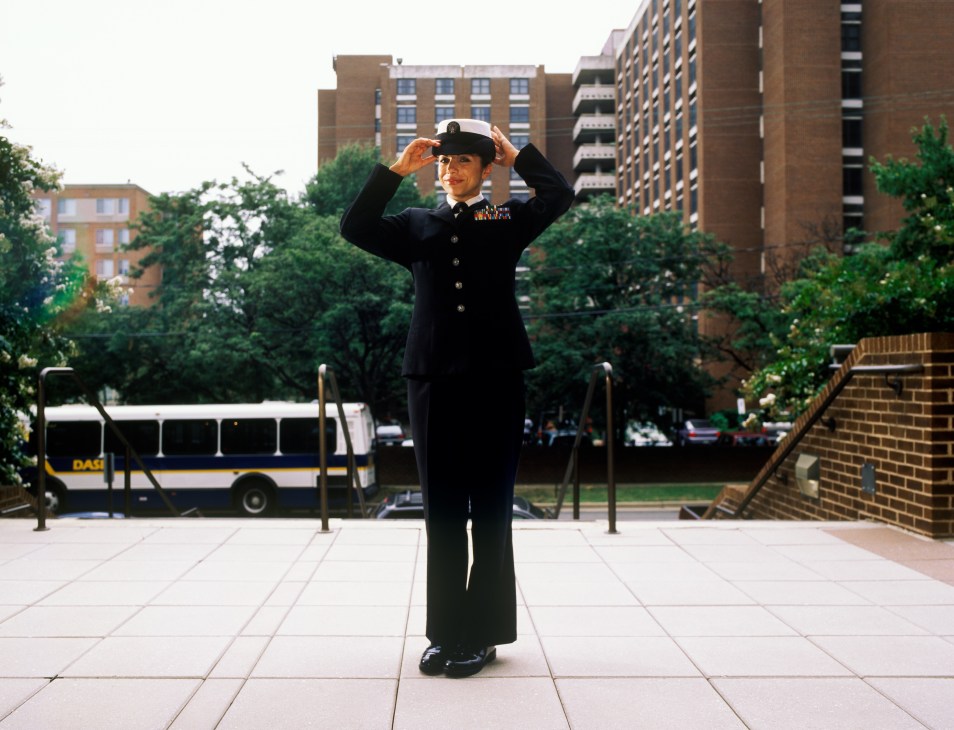 Petty officer Lizandra Murray in Navy uniform adjusting her cap in an urban courtyard setting.
