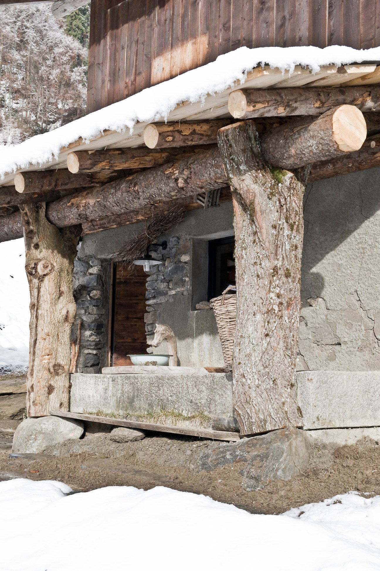 Rustic Alpine barn entrance with weathered wooden beams and stone foundation covered in snow