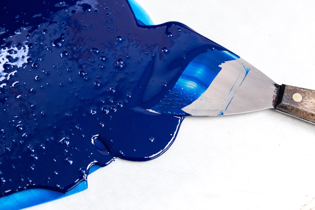 A paintbrush with blue paint being mixed by hand for Pantone fan deck production.
