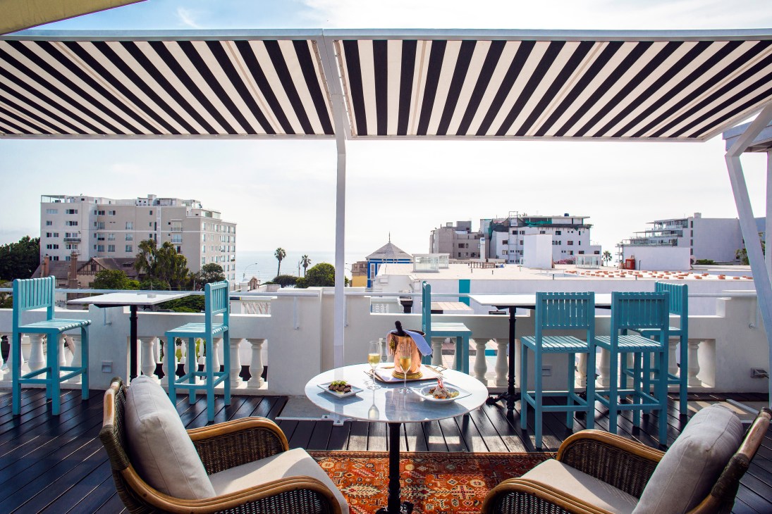 Hotel B's rooftop terrace with striped awning, turquoise chairs, and views of Lima's Barranco district buildings.