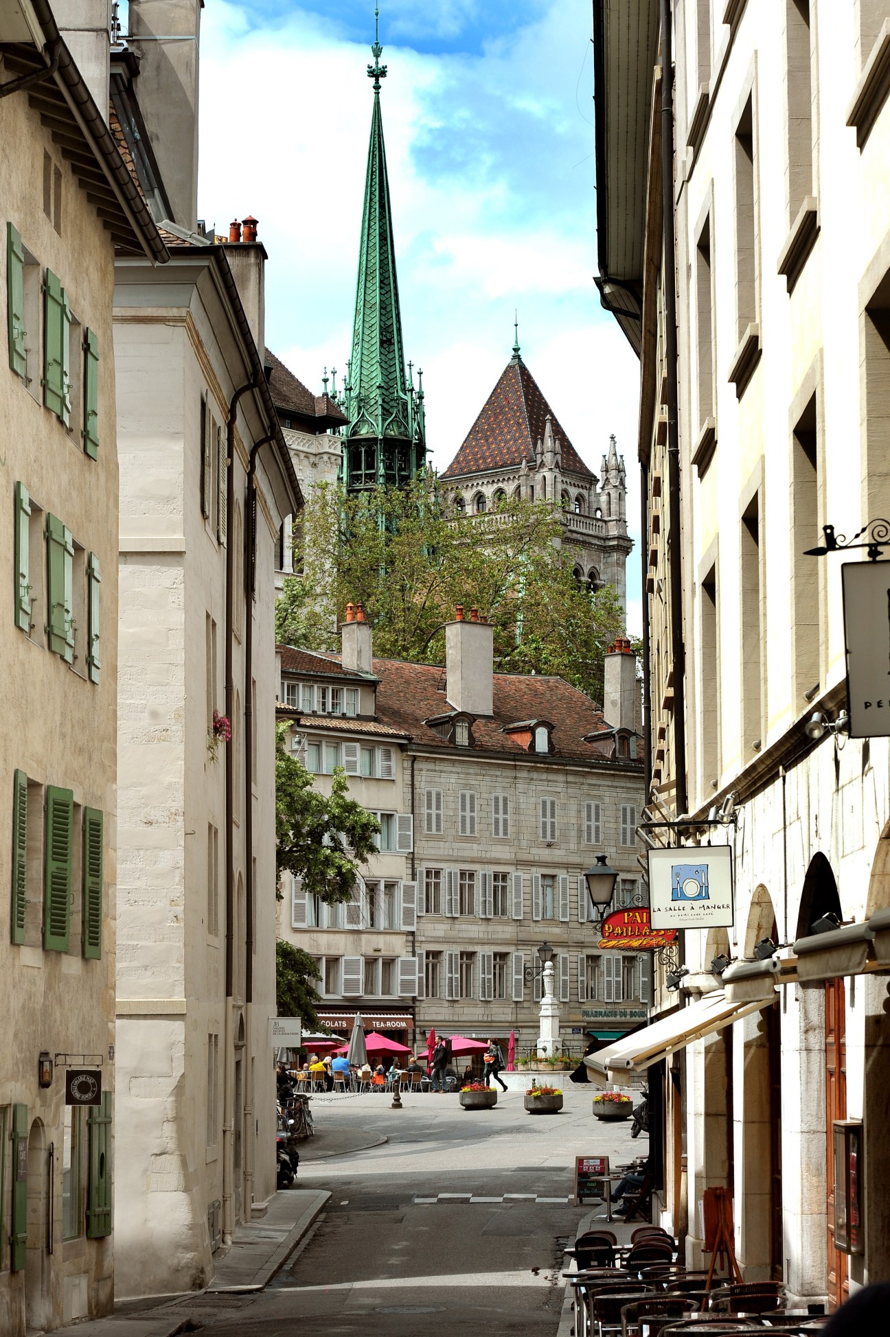 Geneva's Old Town street with historic buildings and a green-spired church in the background.