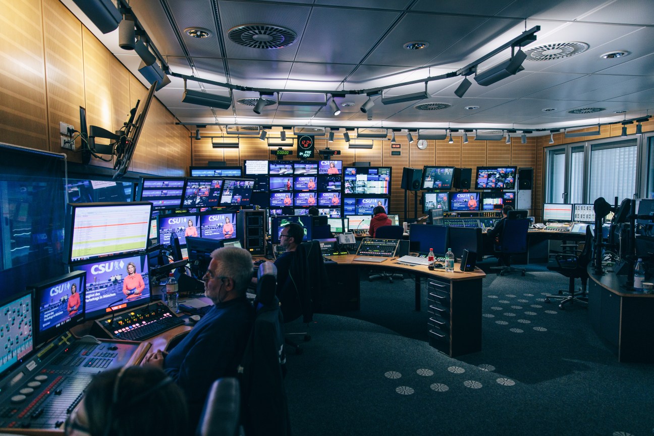The Tagesschau control room during a live newscast with multiple monitors displaying the broadcast and staff operating technical equipment.
