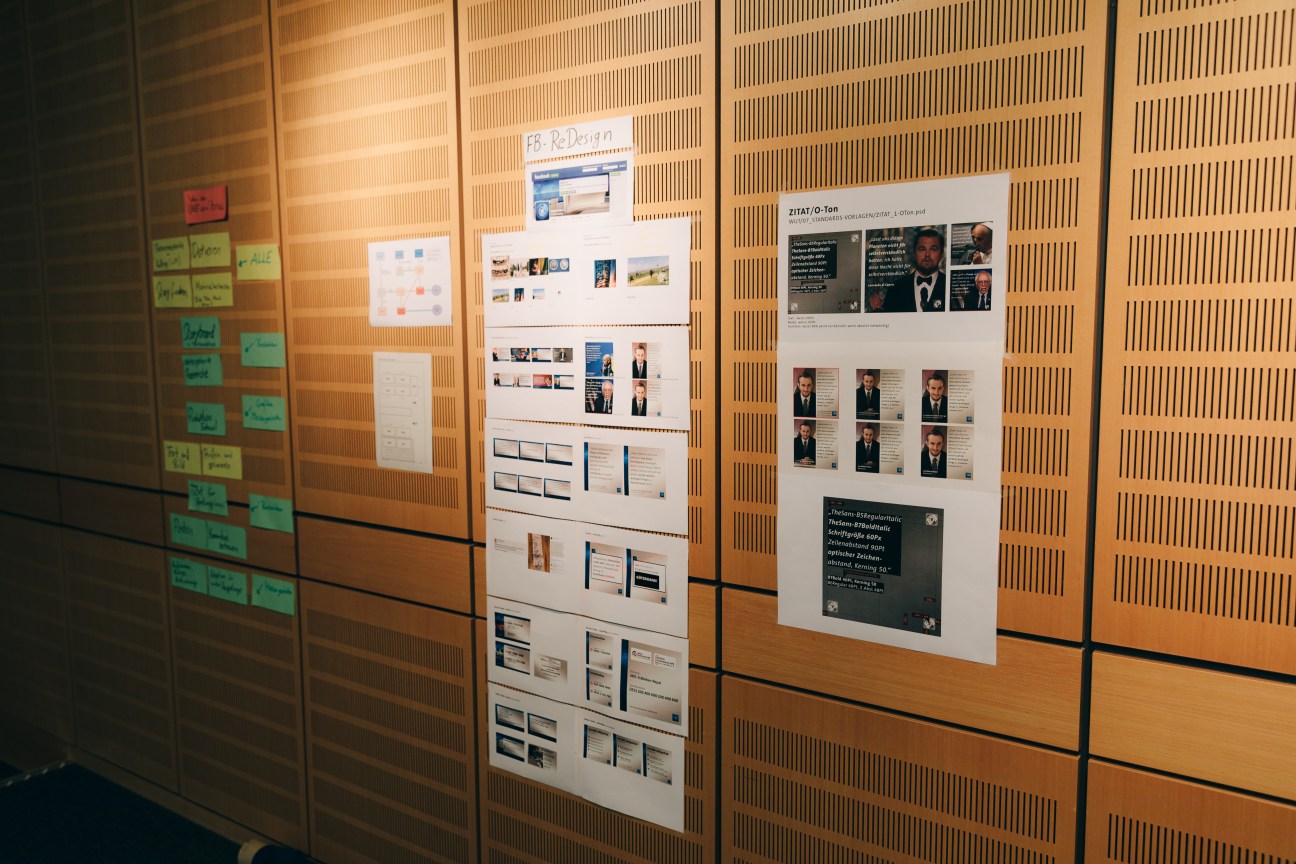 Design boards and mood boards pinned to wooden acoustic panels in a newsroom planning space.