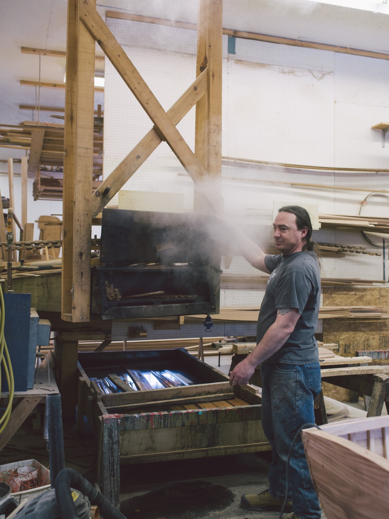 Boatmaker pulling steamed wood strips from a wooden frame structure in workshop.