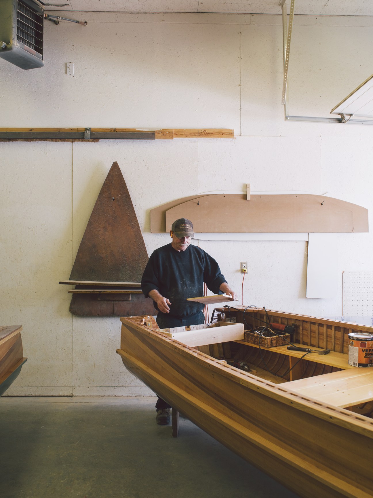 A senior boatbuilder works on wooden boat construction in a workshop.