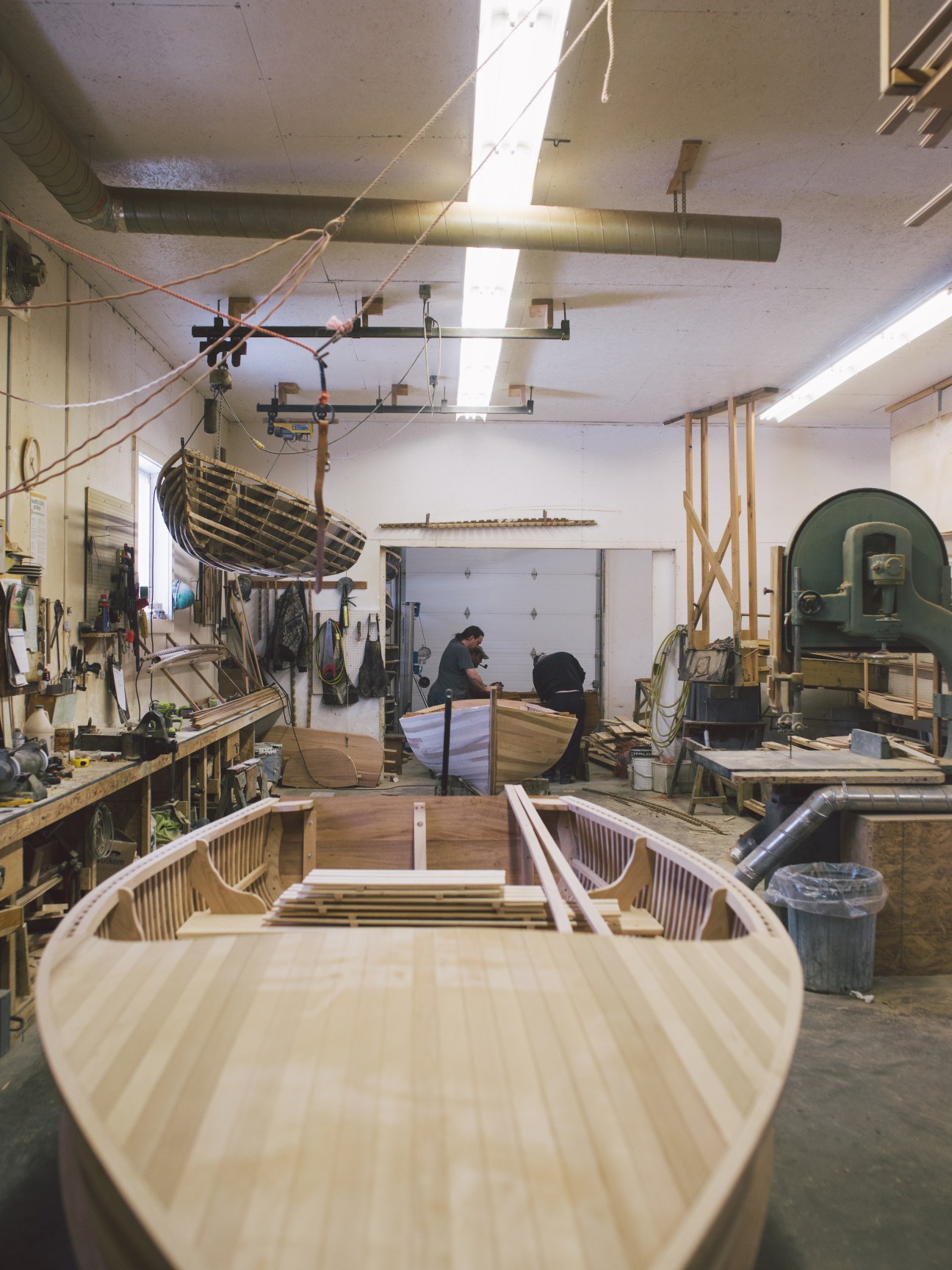 Interior of B Giesler and Sons boat workshop with wooden rowboats under construction and craftspeople working.